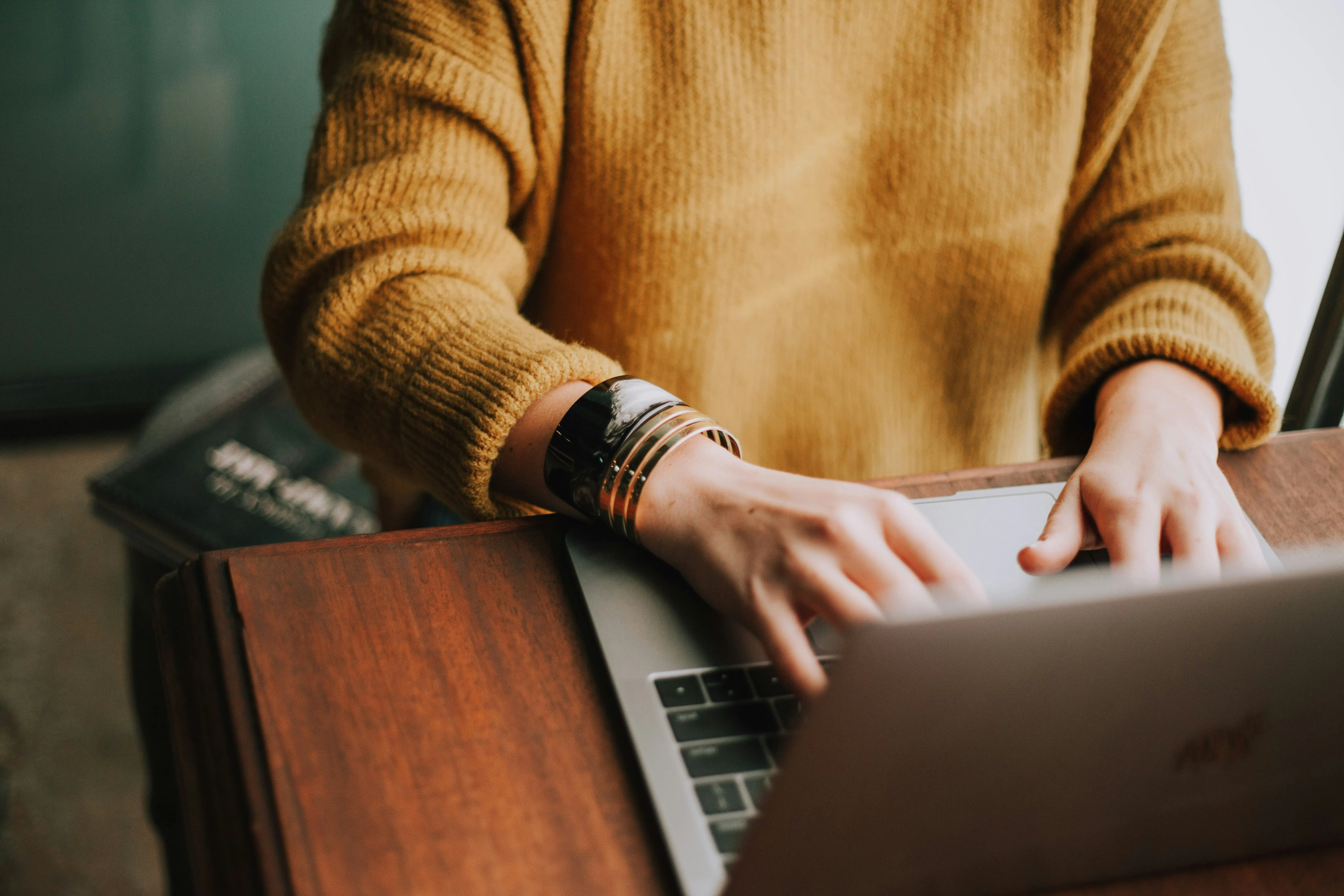Person in a mustard sweater using a laptop at a wooden table